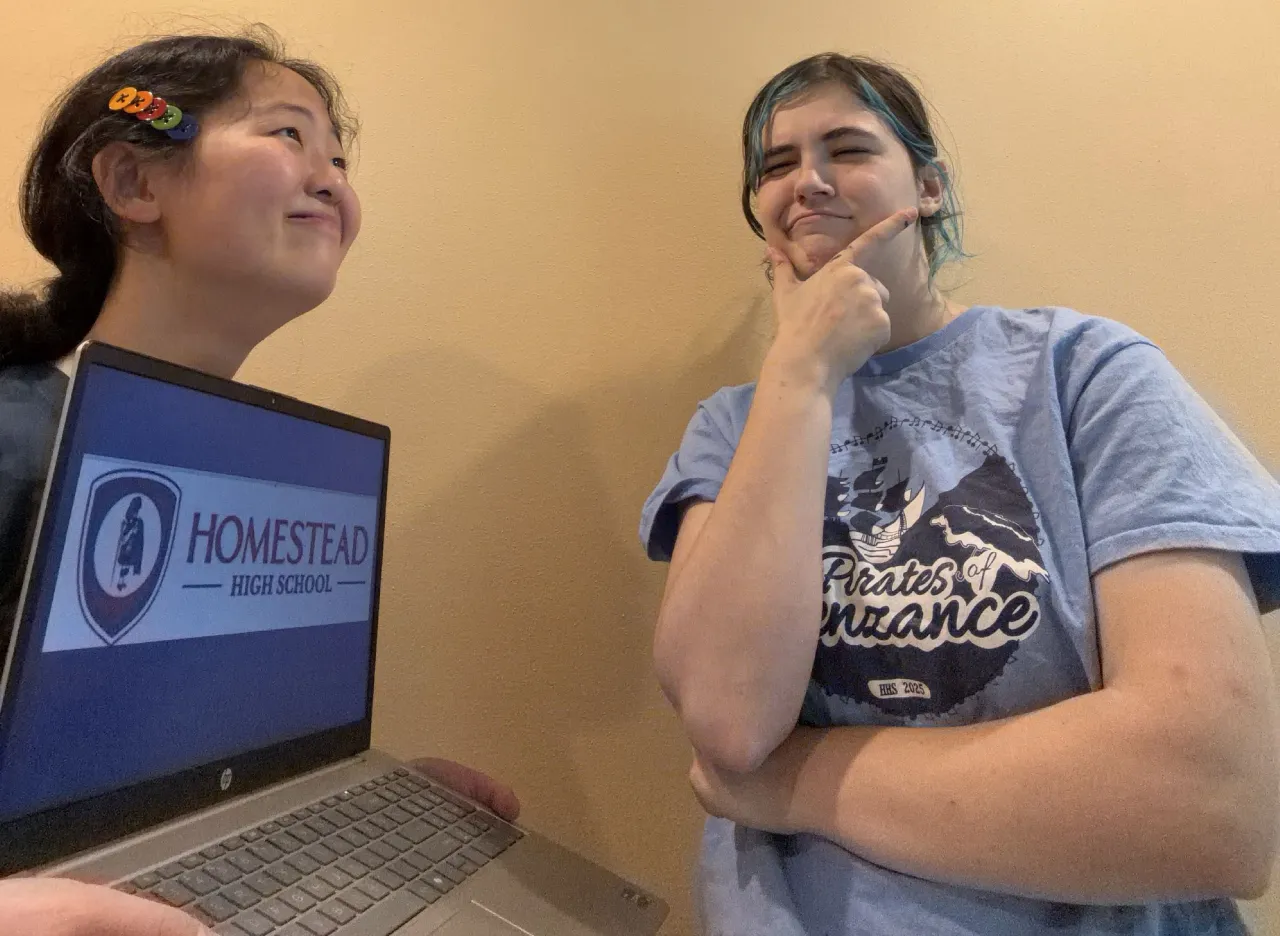 Two club members with a laptop showing their school logo